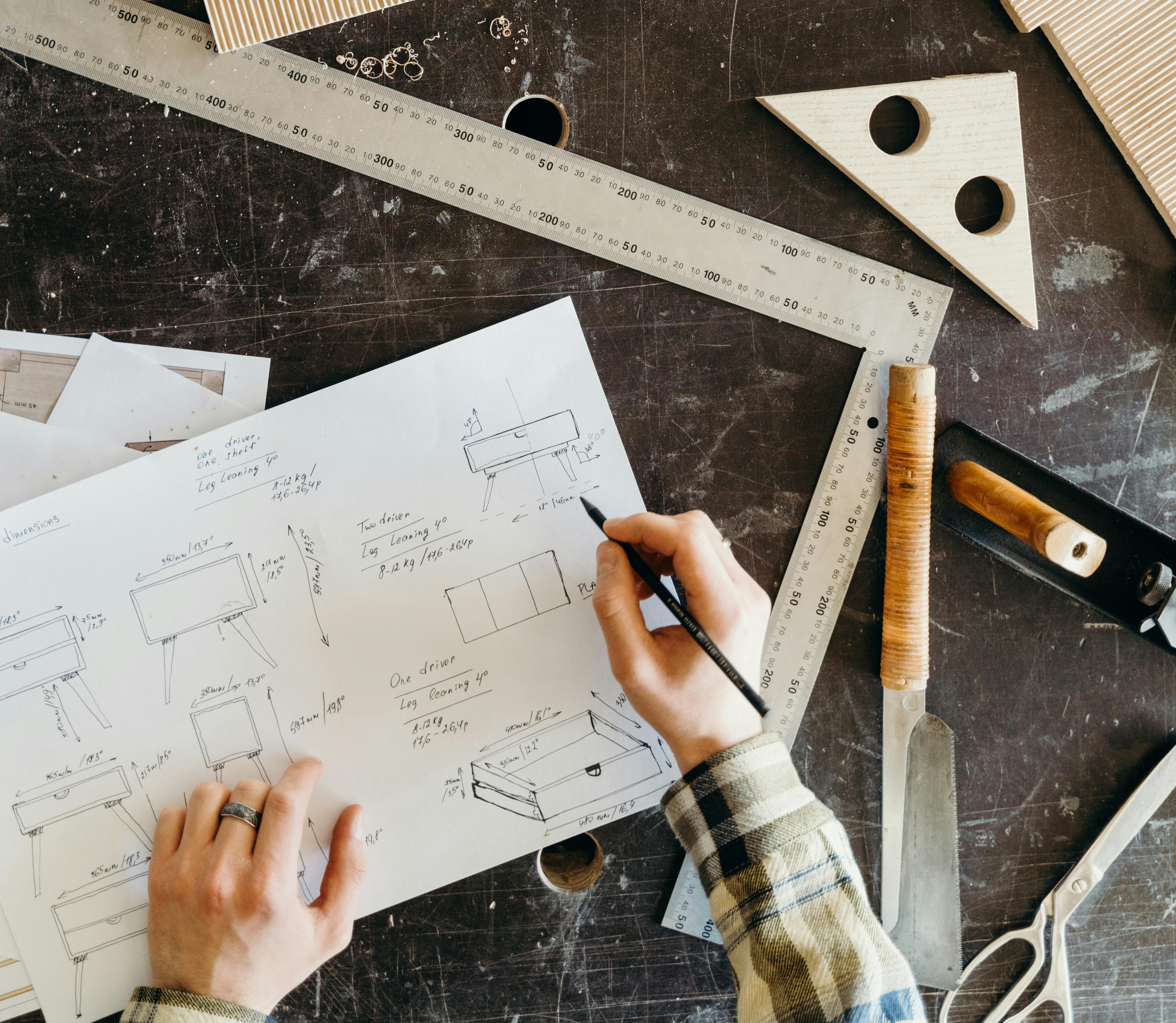 Design — hands sketching product blueprints with rulers and wood samples on workbench